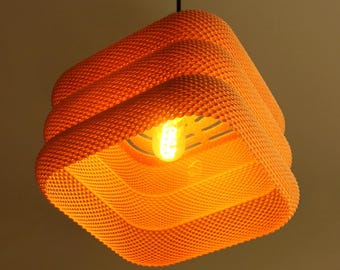 May include: Orange, square pendant light with a textured, dotted surface. The light has a layered design and a visible lightbulb in the centre. The fixture is suspended from a black cord.