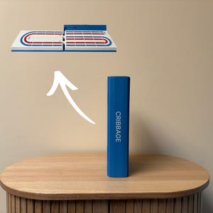 May include: A blue cribbage board game set with a matching blue case. The board is white with red and blue scoring tracks. The case is rectangular and has the word "CRIBBAGE" printed vertically on the side.