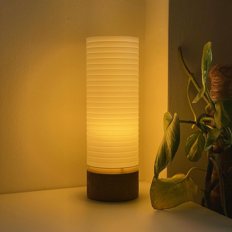 May include: A white table lamp with a wood base and a white ribbed shade. The lamp is turned on and casting a warm glow.