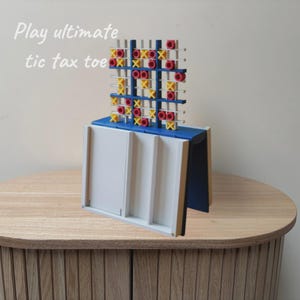 May include: A vertical tic-tac-toe game board featuring a blue frame with a white grid. The game includes yellow X and red O markers. The text "Play ultimate tic tax toe" is visible in the upper left corner of the image.