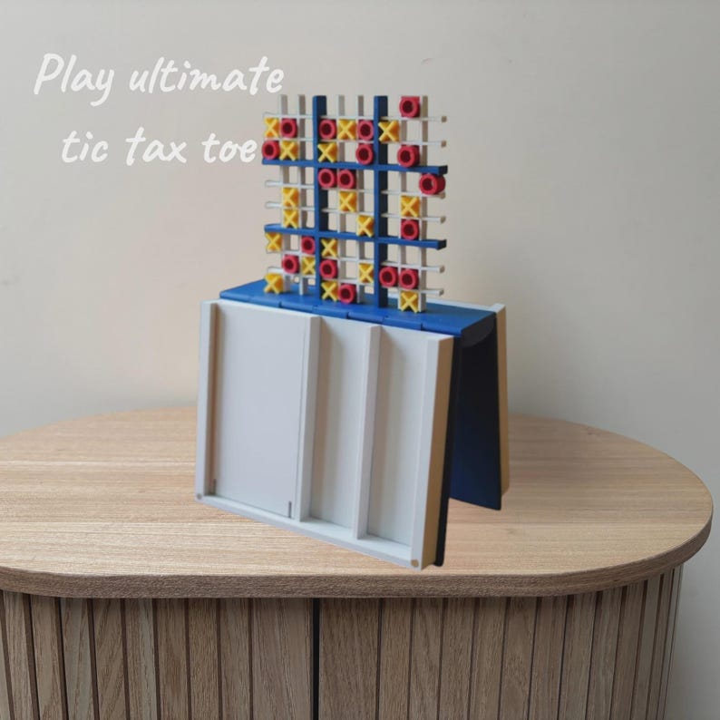 May include: A vertical tic-tac-toe game board featuring a blue frame with a white grid. The game includes yellow X and red O markers. The text "Play ultimate tic tax toe" is visible in the upper left corner of the image.