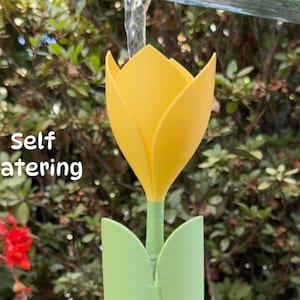 Könnte beinhalten: Ein gelber, tulpenförmiger Selbstbewässerungs-Apparat aus Kunststoff mit grünem Sockel. Der Apparat wird mit einem Wasserstrahl bewässert.