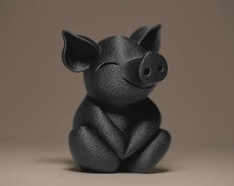 Könnte beinhalten: Eine schwarze Schweinefigur mit geschlossenen Augen und einem Lächeln. Die Figur sitzt mit verschränkten Beinen. Die Oberfläche ist strukturiert. Die Ohren sind aufgestellt. Der Hintergrund ist einfarbig neutral.