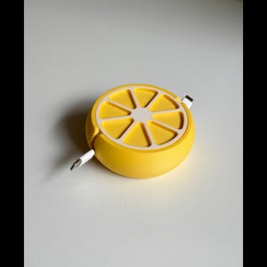 Könnte beinhalten: Ein gelber, limonenförmiger Kabelorganizer mit einer weißen Mitte und einem weißen Kabel, das durch ihn verläuft.