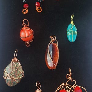 May include: A collection of handmade wire-wrapped pendants and jewelry pieces. The assortment includes pendants with colorful beads, gemstones, and crystals, all crafted with copper wire. The jewelry is displayed against a black background.