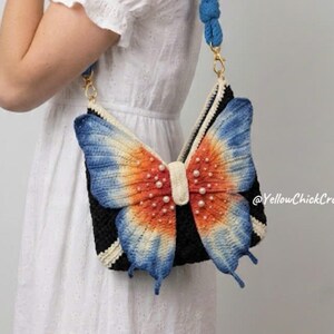 May include: A black crochet handbag featuring a large, three-dimensional butterfly design on the front. The butterfly wings are gradient-colored in orange, yellow, and blue with small white pearl accents. It has a thick blue crochet shoulder strap.