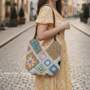 Könnte beinhalten: Bunte Häkeltasche mit Patchwork-Design, mit Quadraten in verschiedenen Farben und Mustern. Die Tasche hat braune Ledergriffe und wird über der Schulter getragen. Im Hintergrund eine Kopfsteinpflasterstraße und Gebäude.