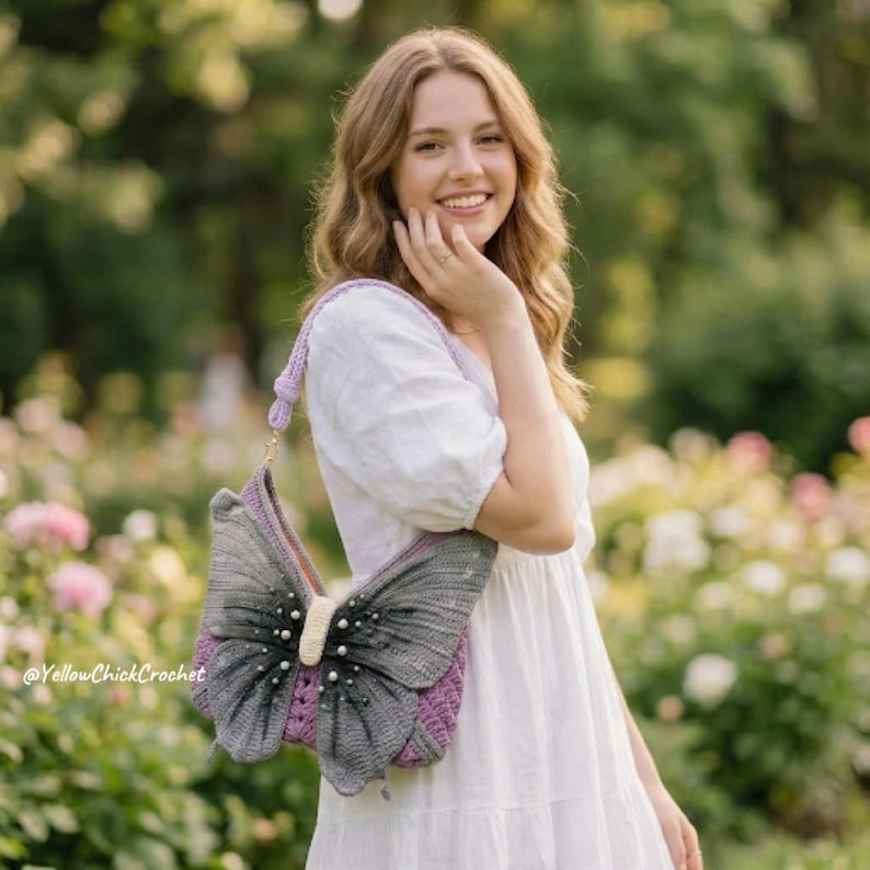 May include: A crochet handbag shaped like a butterfly with dark gray wings, a cream-colored center body, and small white pearl-like accents. The bag features a purple crocheted base and a matching purple shoulder strap. The text @YellowChickCrochet is visible.