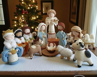 May include: A crocheted nativity scene with figures including the Three Wise Men, Mary, Joseph, an angel, baby Jesus, and animals. The figures are in various colors, including blue, white, brown, and gold. A Christmas tree is in the background.