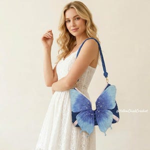 May include: A crochet shoulder bag shaped like a butterfly with gradient blue wings, featuring small white bead accents on the surface, a dark blue base, and a matching braided strap. The text @YellowChickCrochet is visible on the right side.