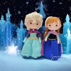 Pode incluir: Duas bonecas de crochê, inspiradas nos personagens de "Frozen", destacam-se contra um fundo nevado e gelado. Uma boneca tem cabelo loiro e um vestido azul-esverdeado, a outra tem cabelo ruivo e um vestido azul. Ambas as bonecas têm capas e pérolas.