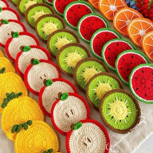 May include: A collection of crocheted fruit-shaped coasters in various colors, including red, green, yellow, and brown. The coasters are arranged in rows and feature designs of watermelon, kiwi, apple, and orange slices.