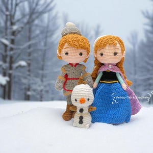 Pu&ograve; includere: Bambole all'uncinetto di personaggi di un popolare film d'animazione. Le bambole includono un personaggio maschile in abito grigio, un personaggio femminile in abito blu e un pupazzo di neve. Le bambole sono ambientate su uno sfondo innevato.