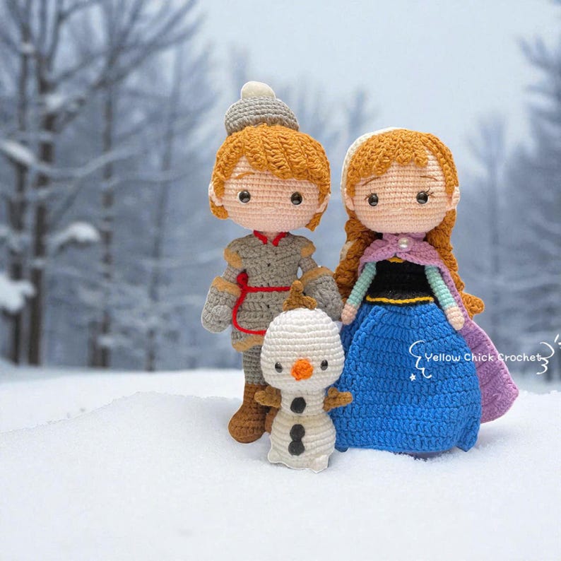 Pu&ograve; includere: Bambole all'uncinetto di personaggi di un popolare film d'animazione. Le bambole includono un personaggio maschile in abito grigio, un personaggio femminile in abito blu e un pupazzo di neve. Le bambole sono ambientate su uno sfondo innevato.