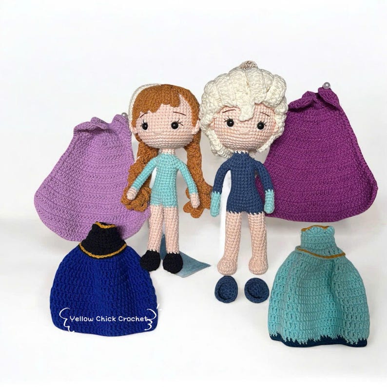 Pu&ograve; includere: Bambole all'uncinetto di due personaggi, una con capelli rossicci e l'altra con capelli bianchi, con abiti blu. Sono presenti anche mantelli e vestiti all'uncinetto in tonalit&agrave; blu e viola. Il testo "Yellow Chick Crochet" &egrave; visibile.