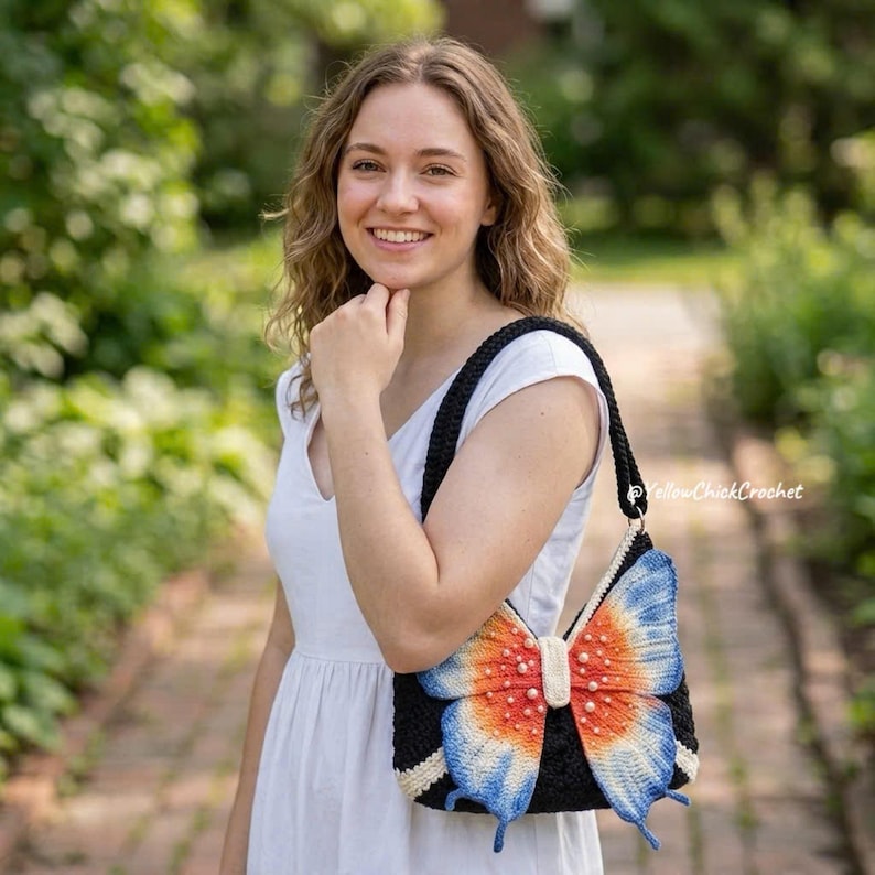 May include: A black crochet shoulder bag featuring a prominent butterfly-shaped applique on the front. The butterfly wings are gradient-colored in orange, white, and blue, accented with small white beads. The bag has a black strap and white trim.