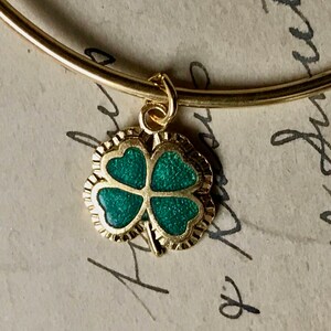 May include: A gold bangle bracelet with a green four-leaf clover charm.