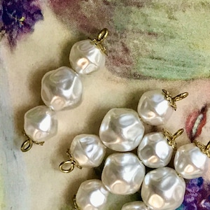 May include: A set of eight white pearl-like beads with gold-toned metal accents. The beads are arranged in two groups of four, with each group forming a cluster.