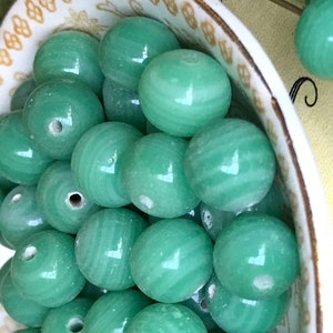 May include: A bowl filled with green jade beads. The beads are round and have a smooth, polished finish. The beads are arranged in a random pattern.