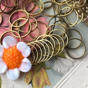 Peut inclure: Un tas d'anneaux de saut en m&eacute;tal dor&eacute;, certains empil&eacute;s et d'autres &eacute;parpill&eacute;s, avec un bouton de fleur blanc et orange au centre.