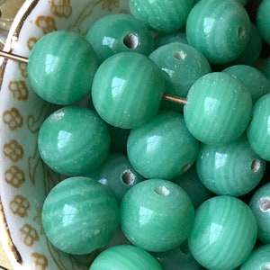 May include: A bowl of green jade beads with a striated pattern. The beads are round and have a smooth, polished finish.