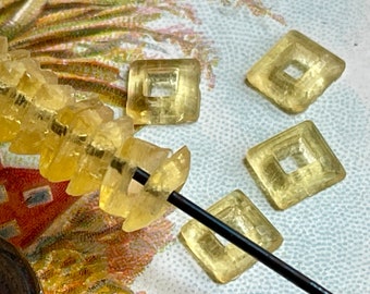 May include: A collection of clear, yellow glass beads with a square shape and a hole in the center. The beads are strung on a black wire and some are scattered on a table with a floral pattern.