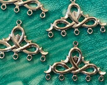 May include: Four silver metal pendant charms with a decorative, intricate design. Each charm has five loops for attaching jewelry findings.