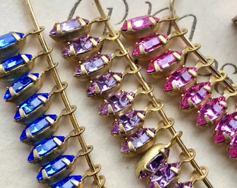 May include: Three strands of gold chain with dangling crystal beads. The beads are in shades of blue, purple, and pink.