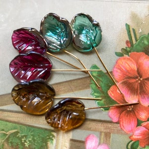 May include: Six glass leaf-shaped embellishments with gold wire stems. The leaves are in shades of green, red, and brown.
