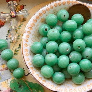 May include: A bowl of green jade beads. The beads are round and have a smooth, polished finish. They are perfect for making jewelry or other crafts.
