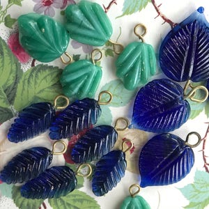 May include: Assortment of blue and green glass leaf charms with gold-toned metal loops. The charms are perfect for jewelry making or crafting projects.