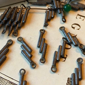 May include: A group of small, silver-colored metal charms, each with a series of three connected bars. The charms have a loop at each end, suggesting they are meant to be attached to a chain or bracelet.