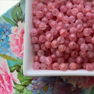 May include: A bowl filled with translucent pink beads. The beads are round and have a frosted finish.