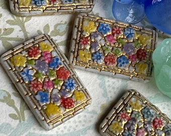 May include: Close-up of several rectangular, floral-patterned buttons with gold trim. The buttons feature a mosaic of colorful flowers in shades of yellow, red, blue, and purple. Also visible are two translucent flower-shaped beads in blue and green.