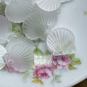 May include: A collection of white, translucent, shell-shaped beads with a hole in the center. The beads are arranged on a white plate with a floral pattern.