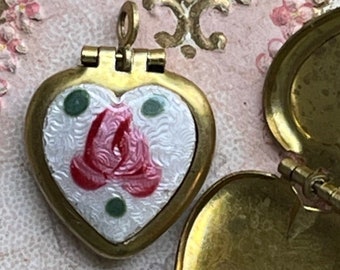 May include: A gold heart-shaped locket with a hinged lid. The locket is decorated with white enamel and a pink rose design. The locket is open, revealing the empty interior.