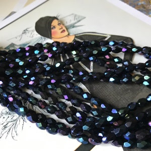 May include: A strand of dark blue iridescent glass beads. The beads are faceted and have a slightly oval shape.