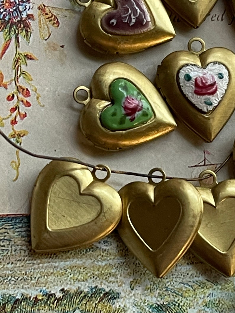 May include: A string of gold heart-shaped locket charms with painted floral designs. Some of the lockets are open and show a blank interior.