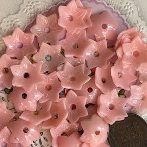 Peut inclure: Une collection de boutons en plastique rose en forme de fleur. Les boutons ont un trou au centre et sont dispos&eacute;s de mani&egrave;re al&eacute;atoire.