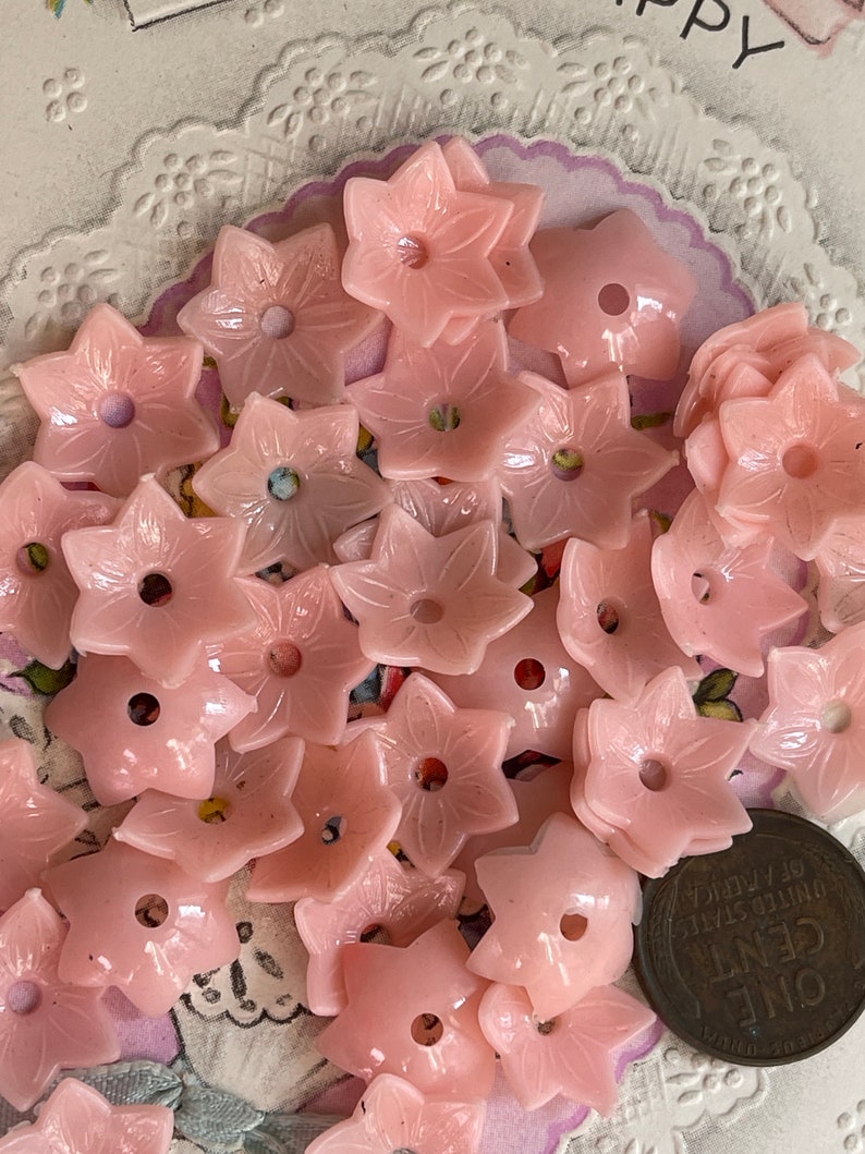 Peut inclure: Une collection de boutons en plastique rose en forme de fleur. Les boutons ont un trou au centre et sont dispos&eacute;s de mani&egrave;re al&eacute;atoire.