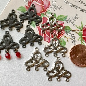 May include: A collection of silver and black metal charms with intricate designs. The charms have three loops at the bottom and a decorative top. Some of the charms have red glass beads attached.