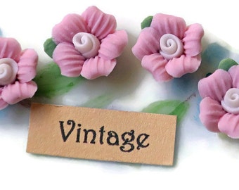 May include: Four pink flower embellishments with white centers, arranged on a white surface with a brown tag that says "Vintage".
