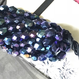 May include: A close-up of a strand of iridescent dark blue faceted glass beads. The beads are strung on black thread.