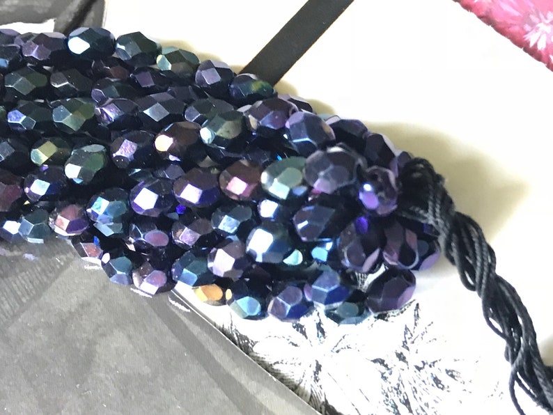 May include: A close-up of a strand of iridescent dark blue faceted glass beads. The beads are strung on black thread.