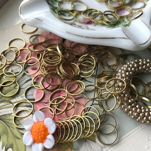Peut inclure: Un grand tas d'anneaux de saut dor&eacute;s, une petite fleur blanche avec un centre orange et un bracelet en perles beige.