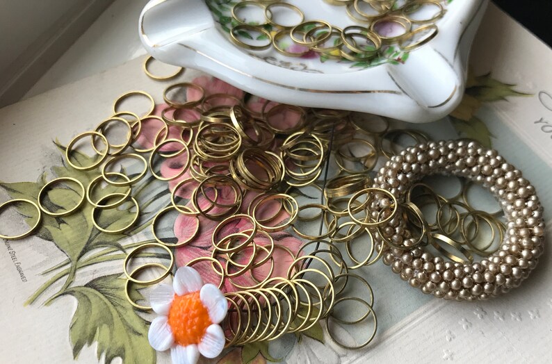 Peut inclure: Un grand tas d'anneaux de saut dor&eacute;s, une petite fleur blanche avec un centre orange et un bracelet en perles beige.