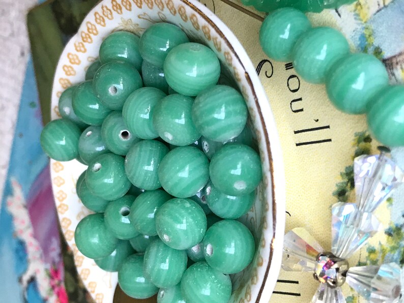 May include: A bowl filled with green jade beads. The beads are round and have a smooth, polished finish. The beads are arranged in a random pattern.