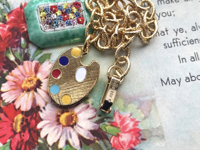 K&ouml;nnte beinhalten: Eine goldene Kettenkette mit einem Anh&auml;nger in Form eines gr&uuml;nen und wei&szlig;en Mosaik-Bilderrahmens und einem goldenen Malpalette-Anh&auml;nger mit bunten Emaille-Farbtupfern. Die Kette hat einen Verschluss mit der Aufschrift "Made in Italy".
