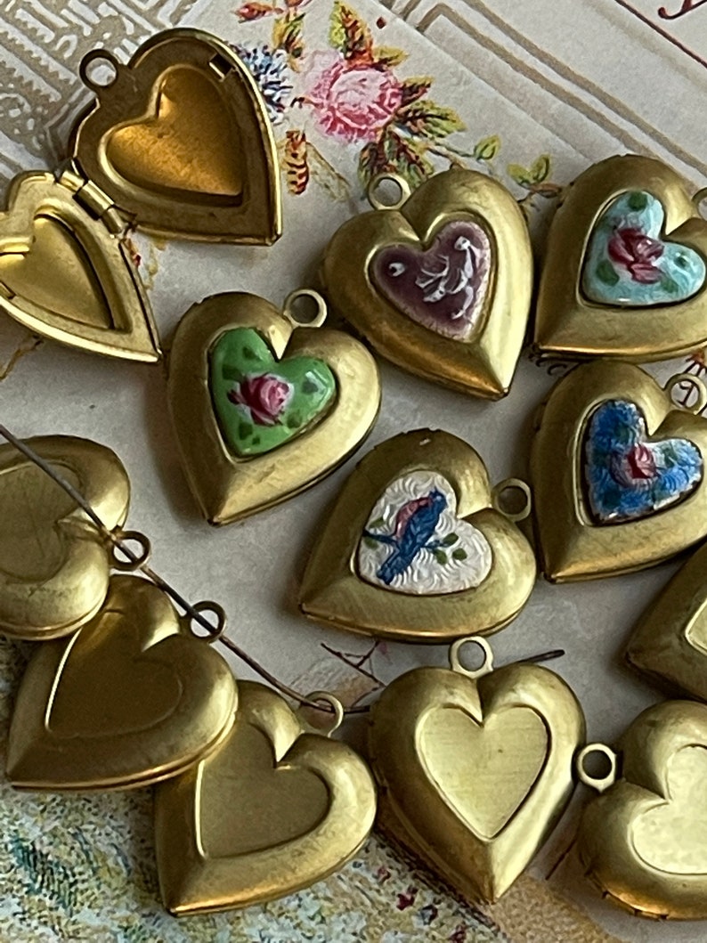 May include: A collection of 10 gold heart-shaped locket pendants with various painted designs. Some lockets feature floral designs, while others have birds or other motifs. The lockets are arranged on a patterned surface.
