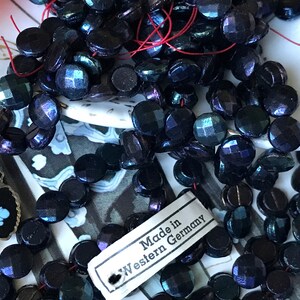 Puede incluir: Una hebra de cuentas de vidrio negro iridiscente con acabado facetado. Las cuentas est&aacute;n enhebradas en un hilo rojo y tienen una etiqueta que dice "Made in Western Germany".